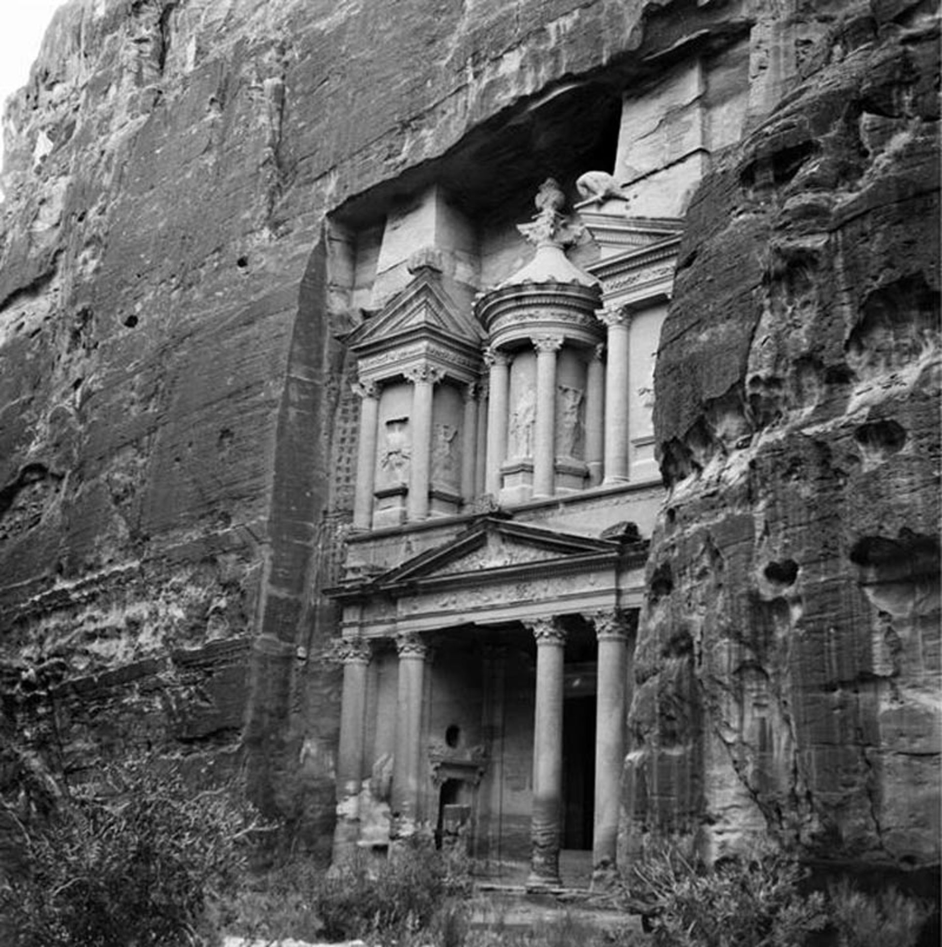 عکس سیاه و سفید از نمای صخره‌ای الخزانه‌داری در شهر باستانی پترا که در دل کوه تراشیده شده