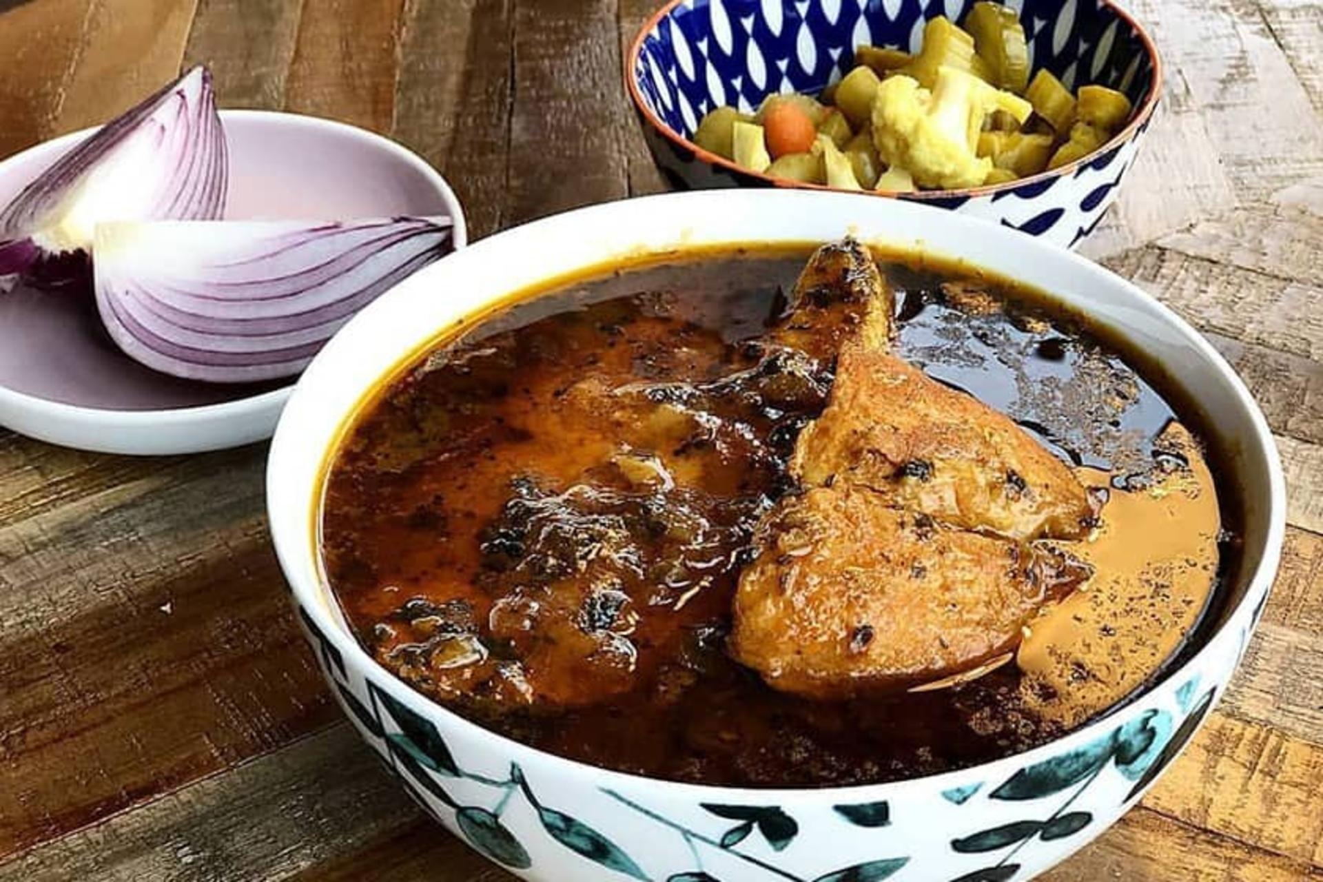یک کاسه قلیه ماهی در کنار شوری و پیاز