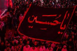 پرچم بزرگ یا حسین در میان جمعیت زیادی از عزاداران در نورپردازی قرمز