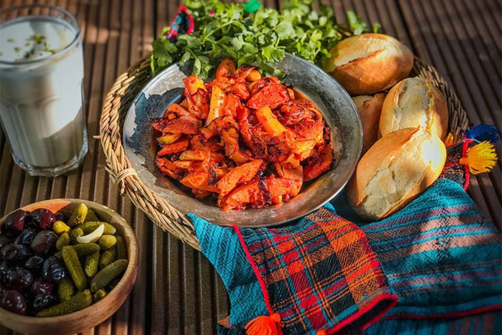 یک ظرف غذا در سبدی از نان و سبزی همراه با دوغ و خیارشور و زیتون