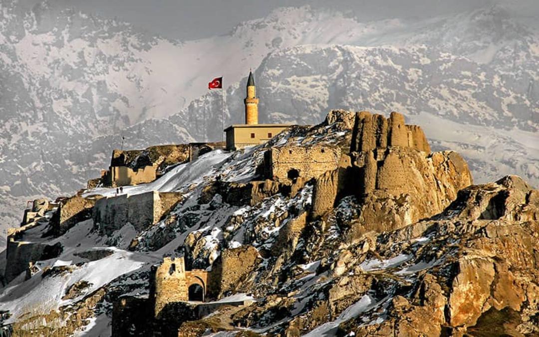 قلعه ای قدیمی در بالای کوه و در کنارش پرچم قرمز ترکیه
