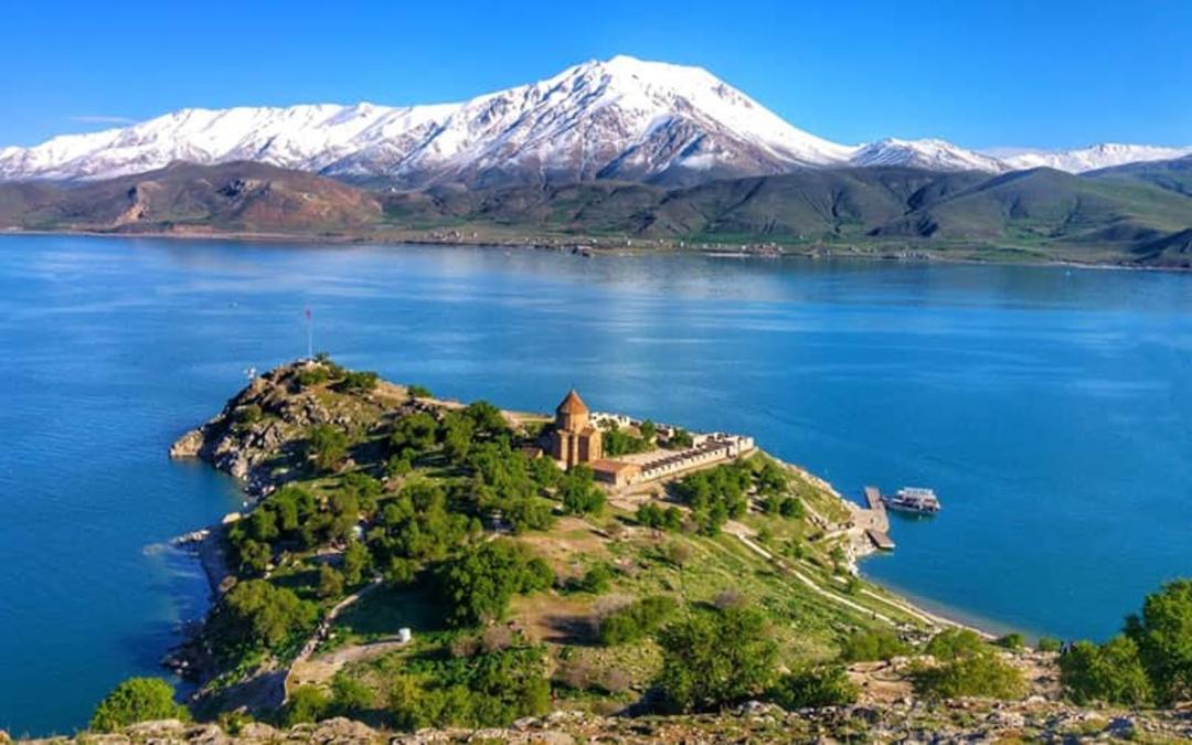 ساختمانی قدیمی در کنار دریاچه با دورنمای کوهی پر از برف
