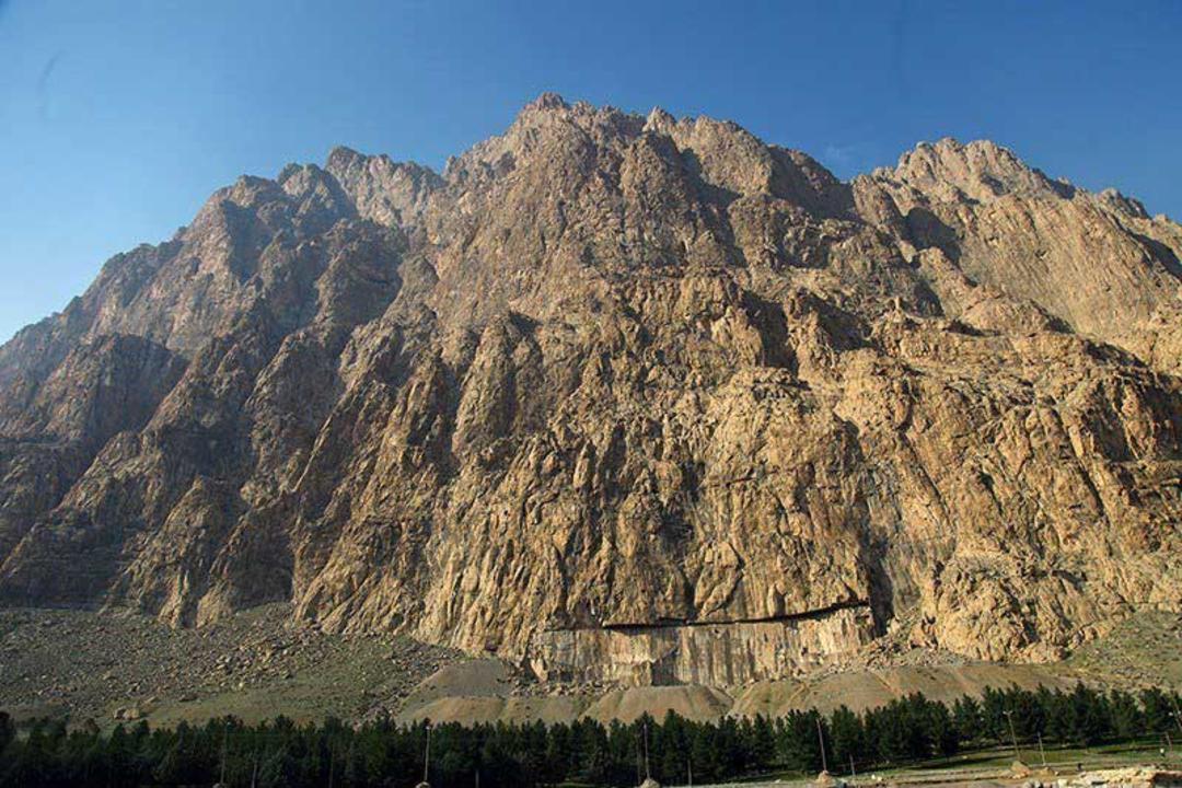 کوه تاریخی بیستون بر فراز درختان سرسبز دامنه‌اش