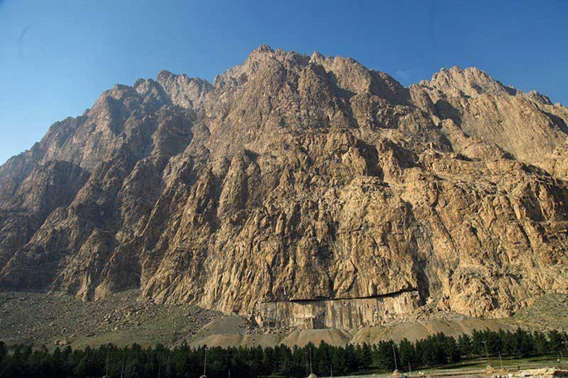 کوه تاریخی بیستون بر فراز درختان سرسبز دامنه‌اش