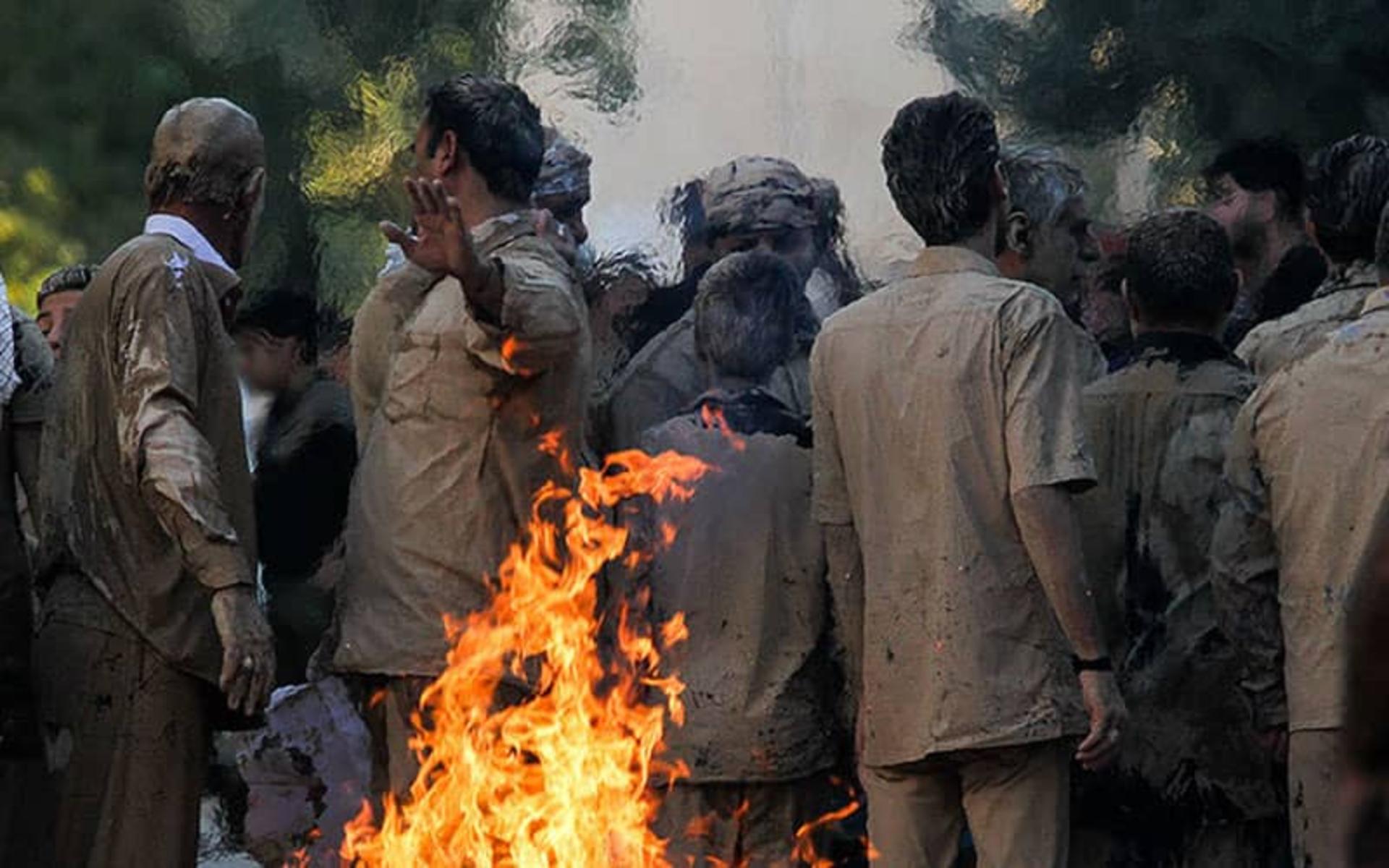ایستادن مردانی با لباس گلی به دور آتش