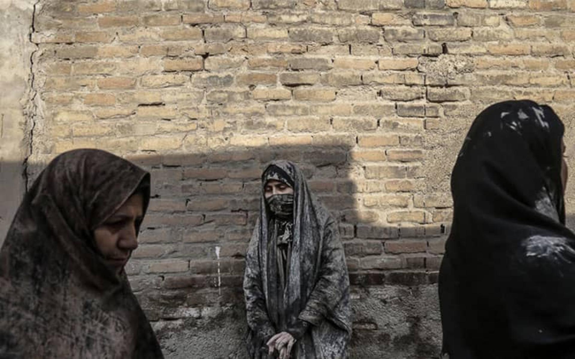 زنی با چادر گلی در کنار دیواری آجری