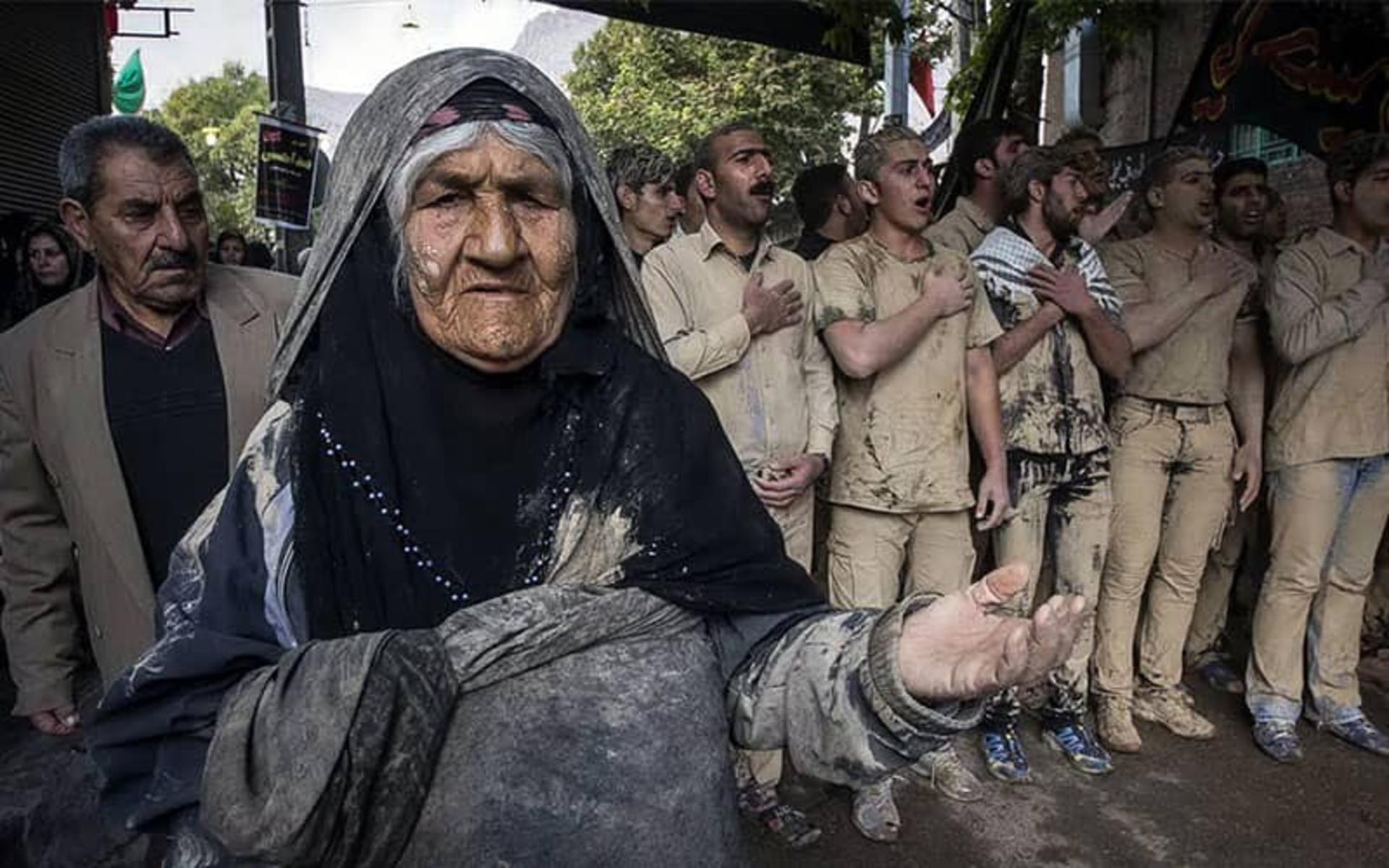 پیرزنی با لباس و صورت گلی و عزاداران مرد با پوشش گلی