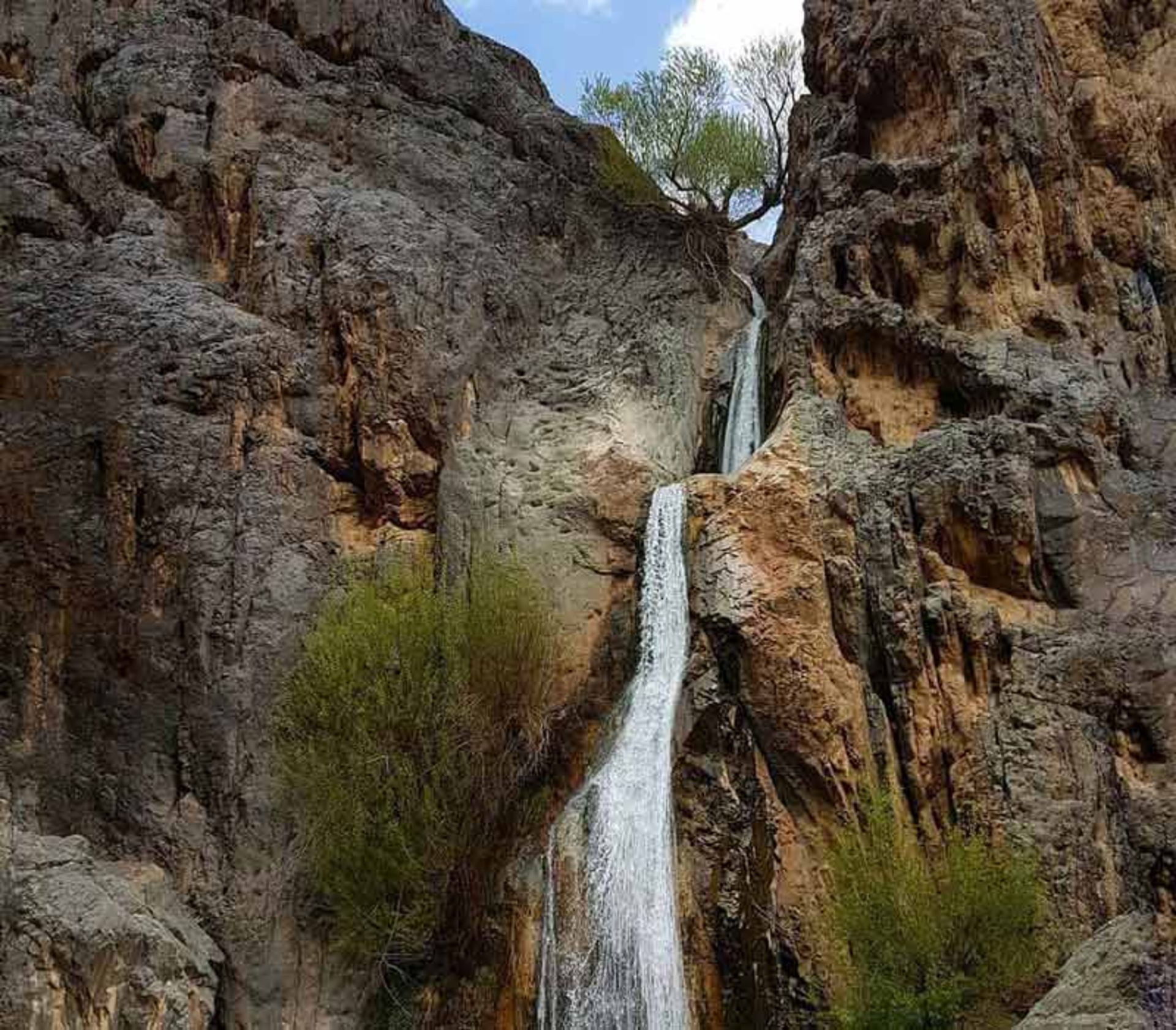 آبشار طامه میان صخره های کوهستانی و درختان سبز