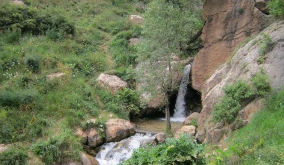آبشار لاسک در مسیر دره لاسک میان بوته های سرسبز و صخره ها