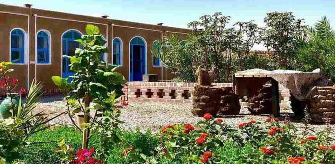 حیاط اقامتگاه بومگردی گندم بریان شهداد با میز و صندلی سنگی و باغچه پر گل