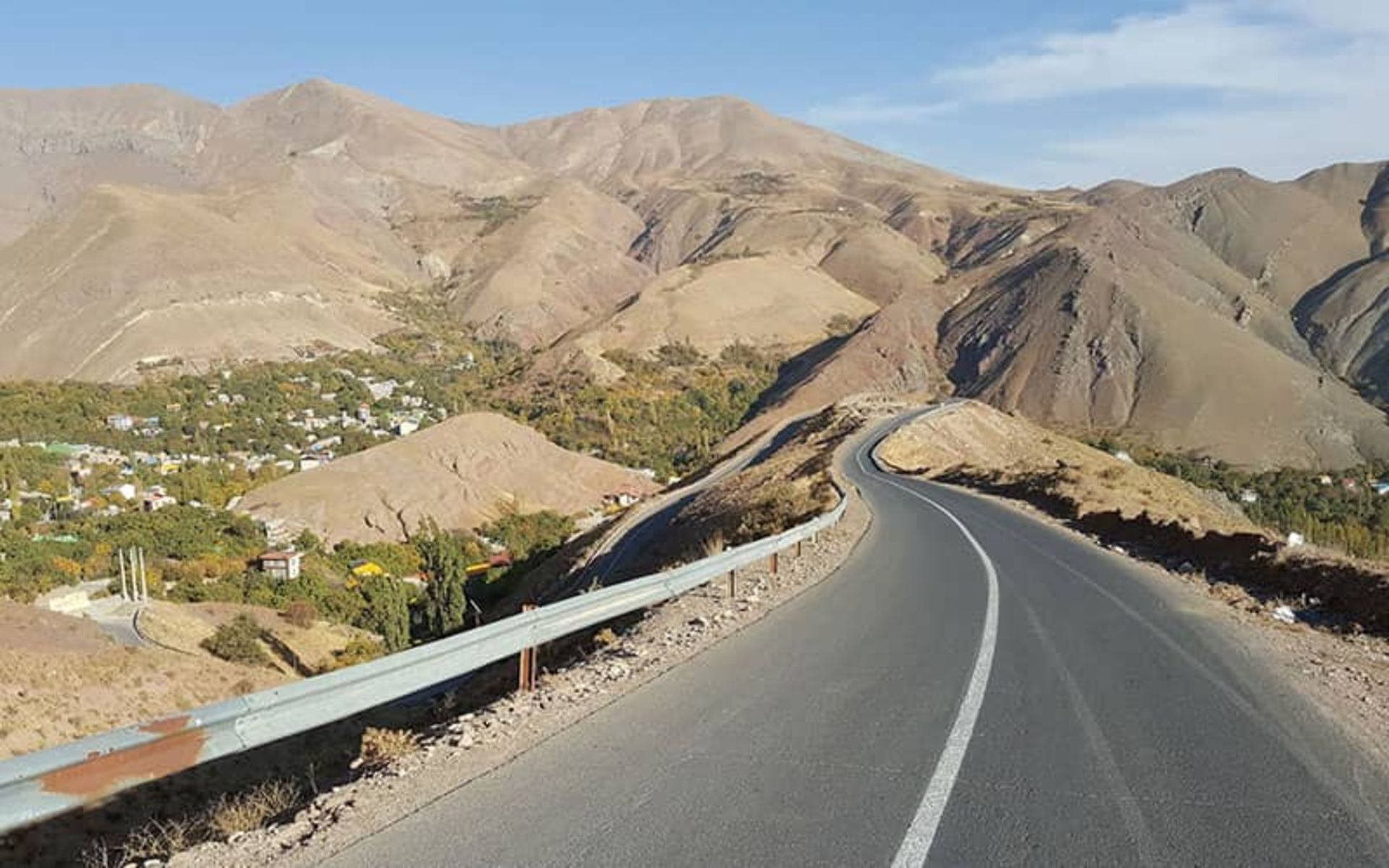 جاده آسفالت در منطقه ای کوهستانی و در کنار روستایی سرسبز