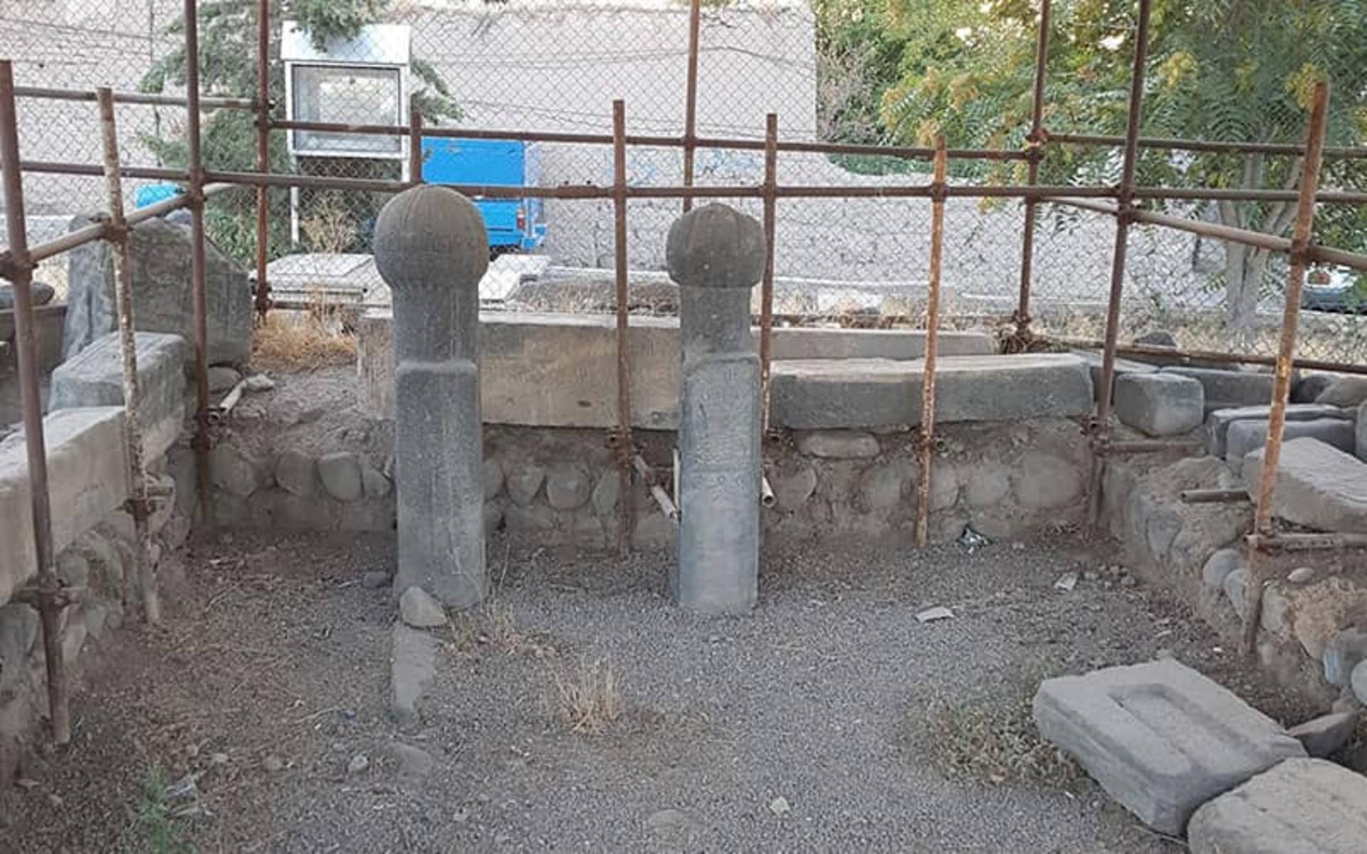 دو ستون سنگی کوتاه و چند قطعه سنگ در محیط دارای فنس