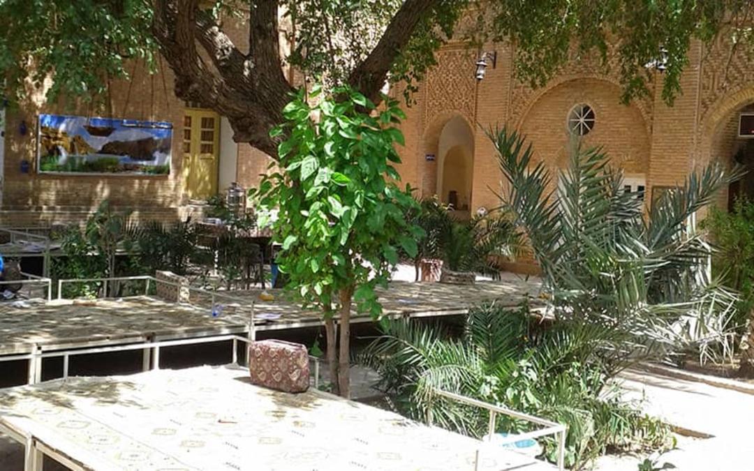 حیاط خانه ای قدیمی با درخت و تخت چوبی