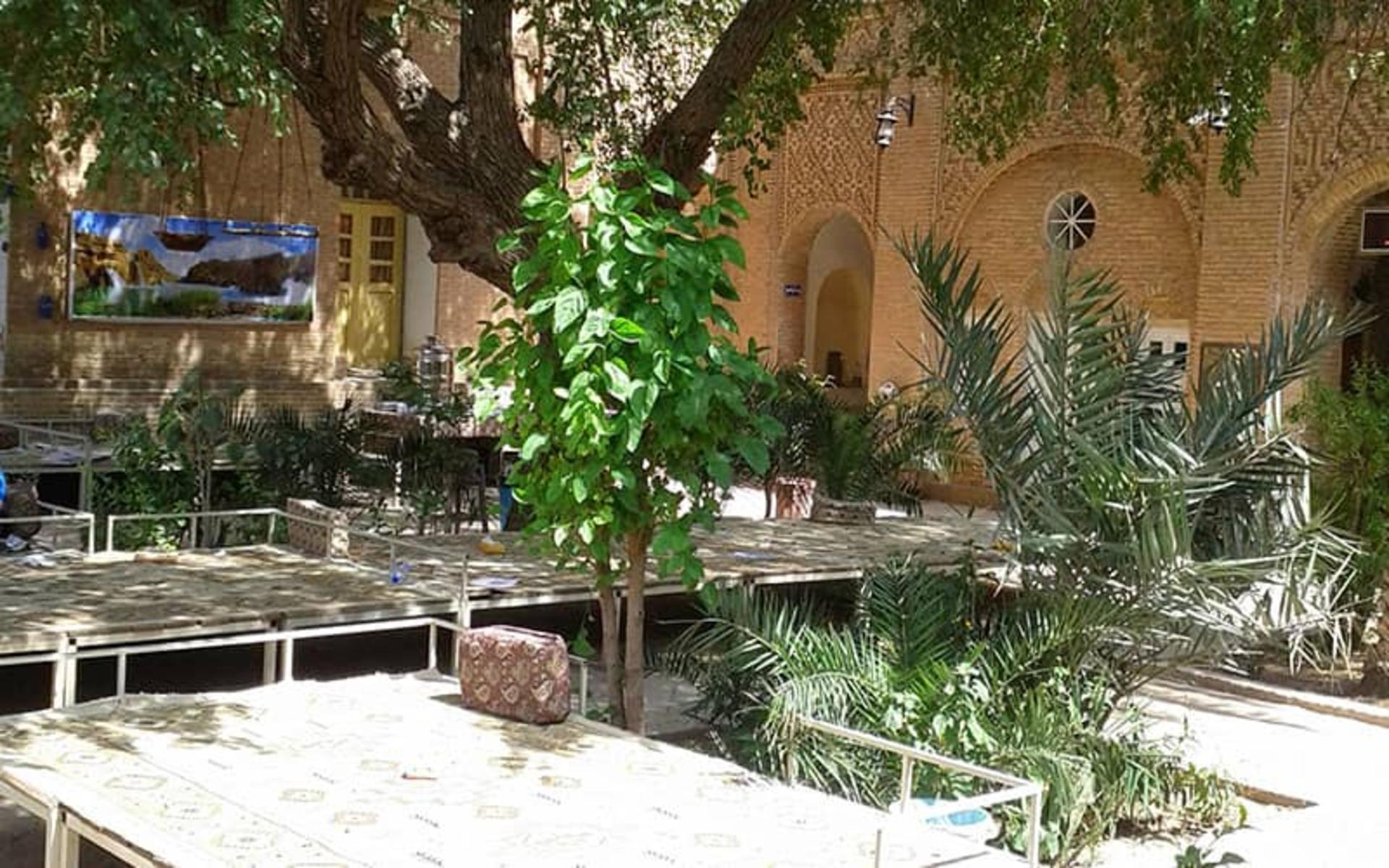 حیاط خانه ای قدیمی با درخت و تخت چوبی