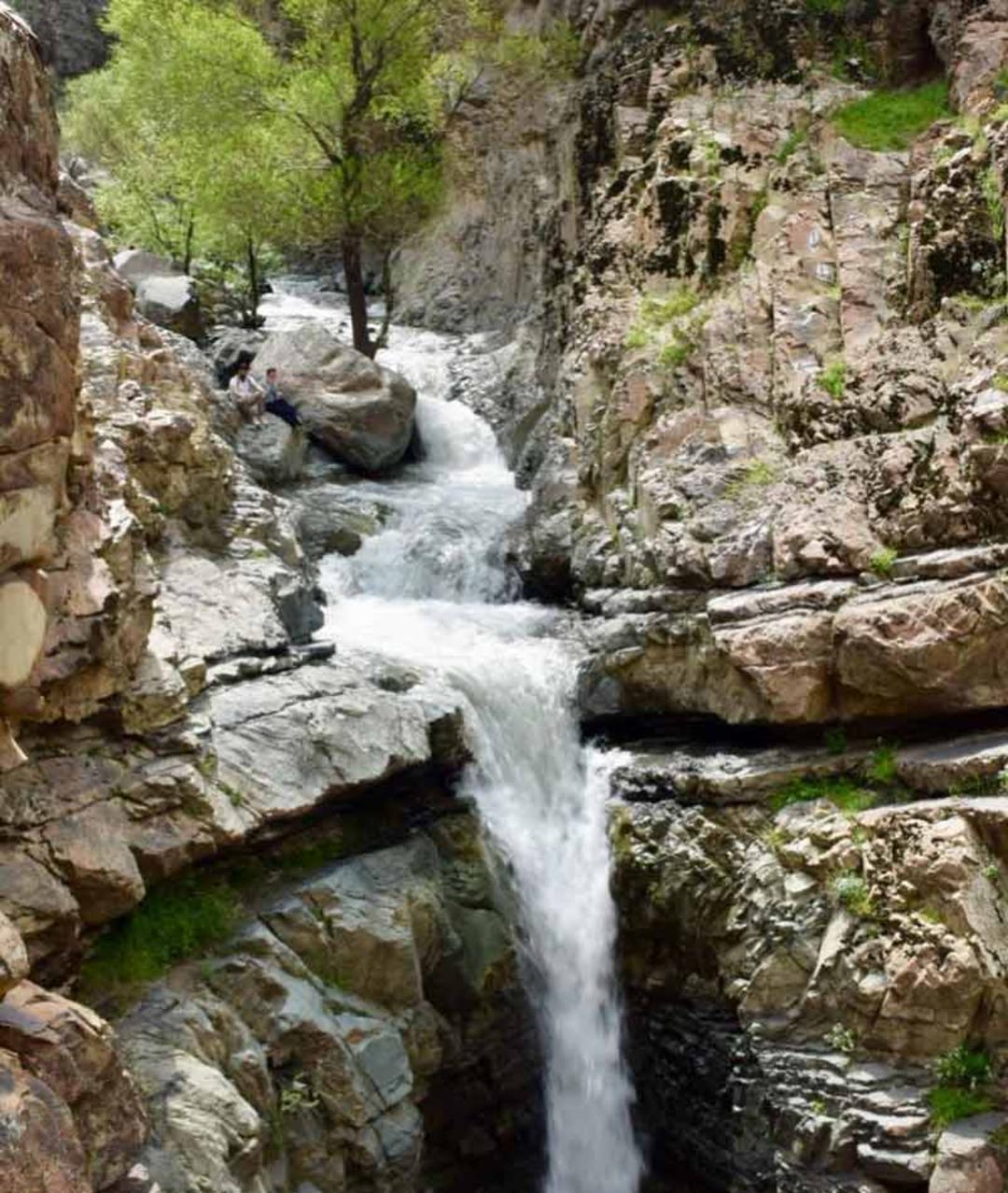 آبشار کبوترخوان میان صخره های لایه ای و سرسبز کوهستانی