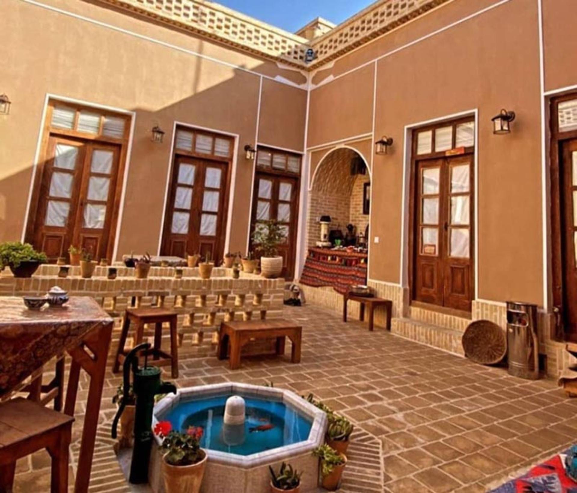 حیاط هاستل واحه یزد با حوض فیروزه ای و پنج دری