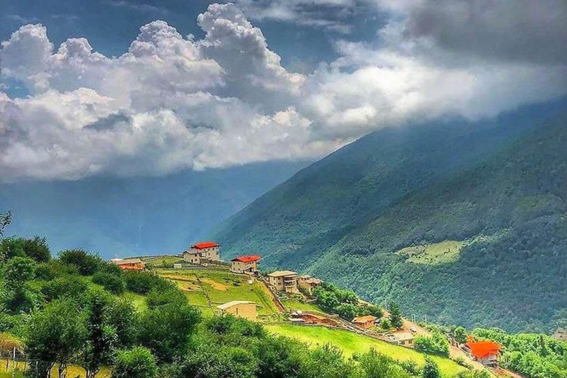 خانه های روستای فشکور بر کوه های سرسبز زیر آسمان ابری با چشم انداز کوهستانی، منبع عکس: صفحه اینستاگرام shomal_foshkour
