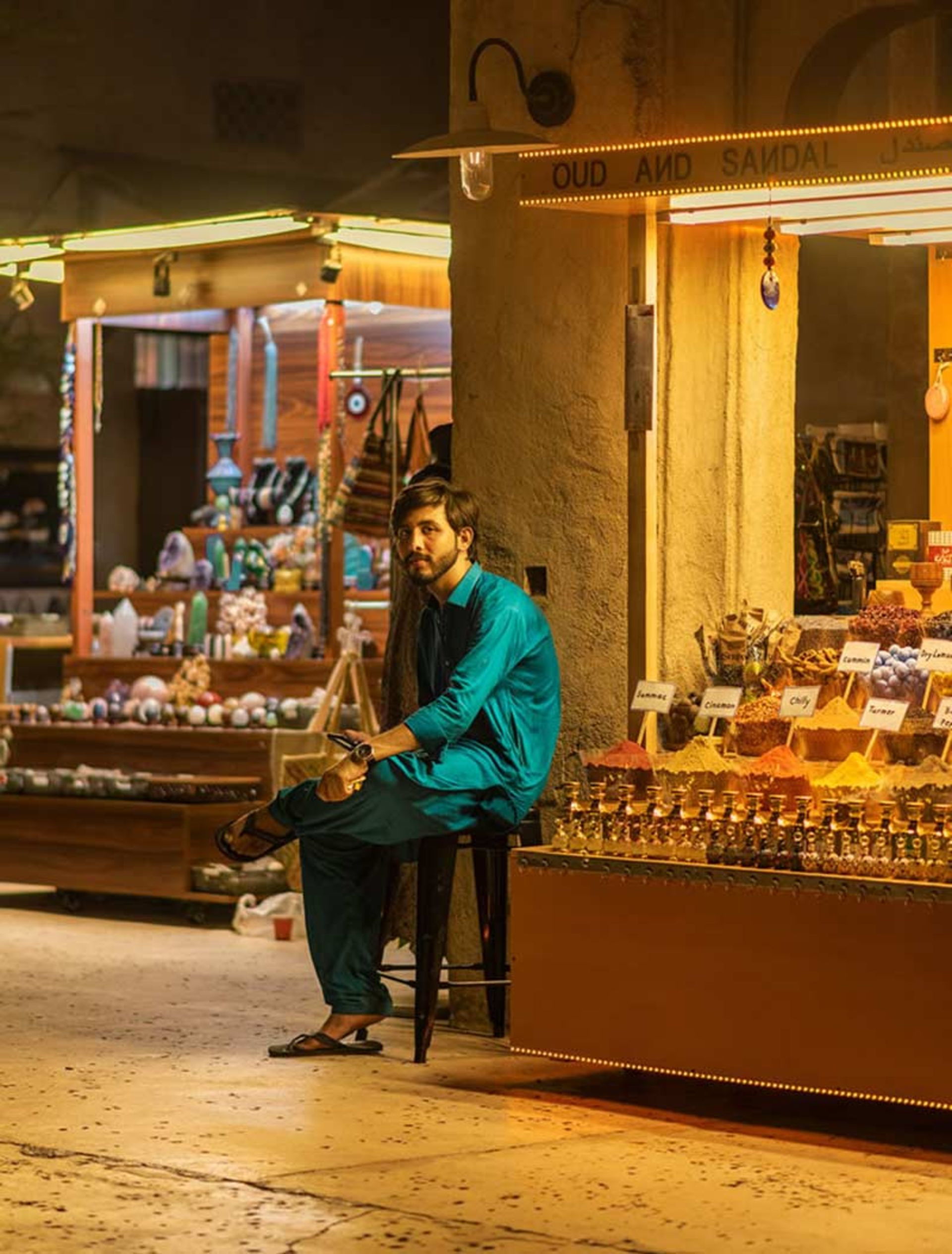مرد عرب با لباس سبزآبی نشسته جلوی مغازه
