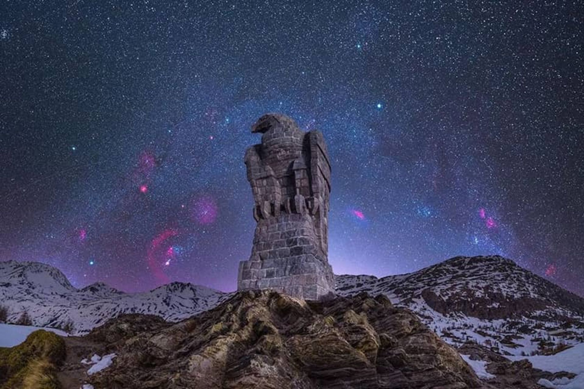 آسمان شب در پس عقابی سنگی در کوهستان برفی