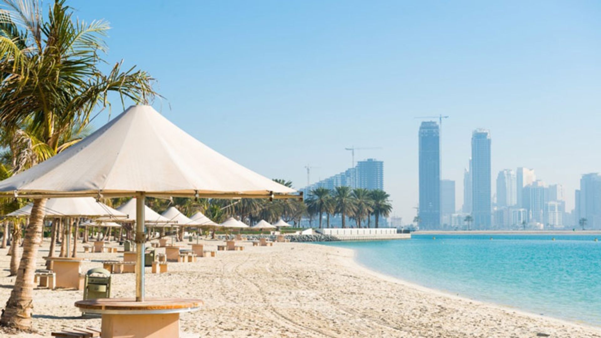 ساحل الممزر دبی با چترهای سایه بان و درختان نخل؛ منبع عکس: Novotel Sharjah Expo Centre
