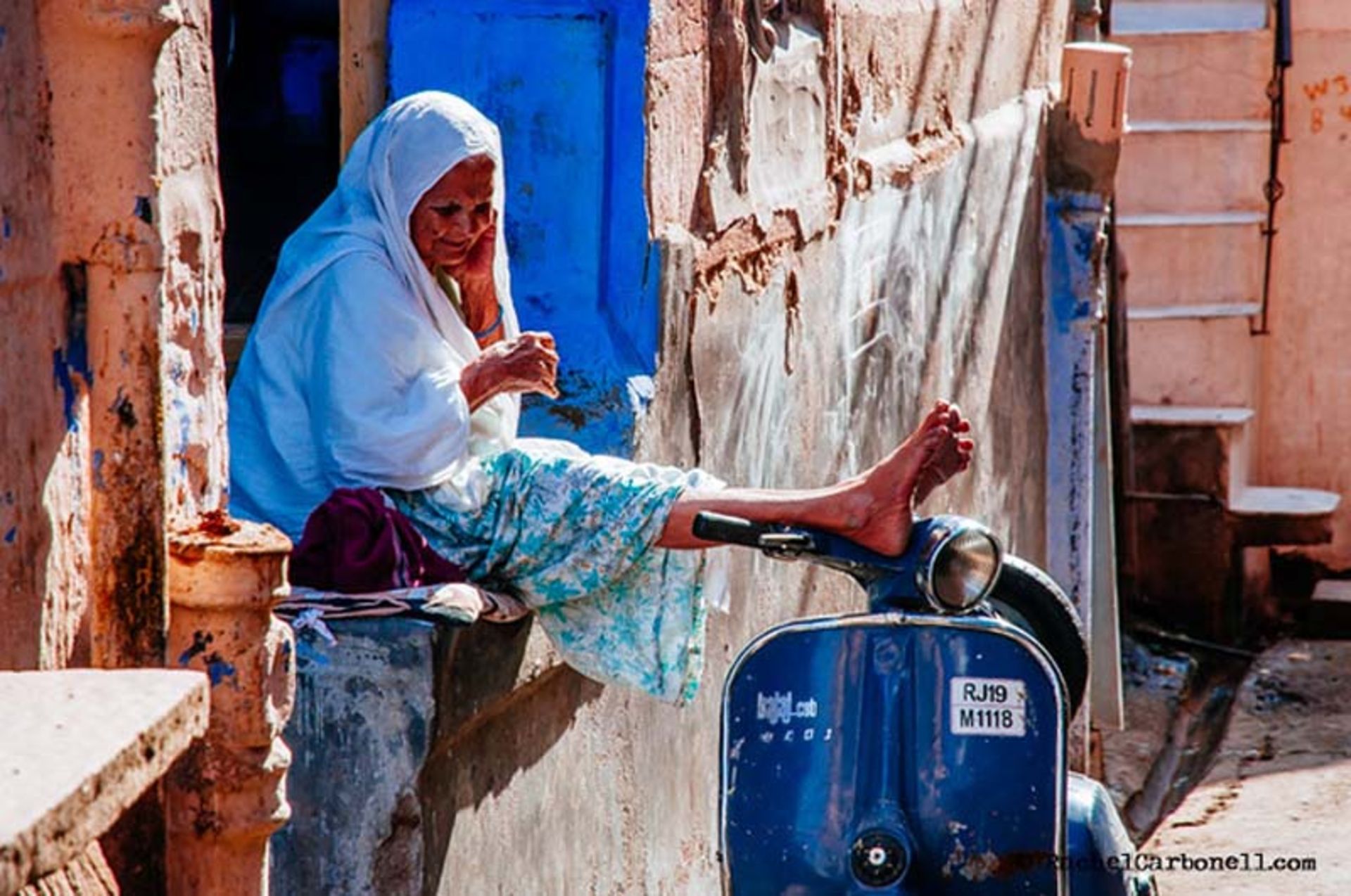 پیرزنی نشسته بر سکویی در کوچه‌های آبی راجستان