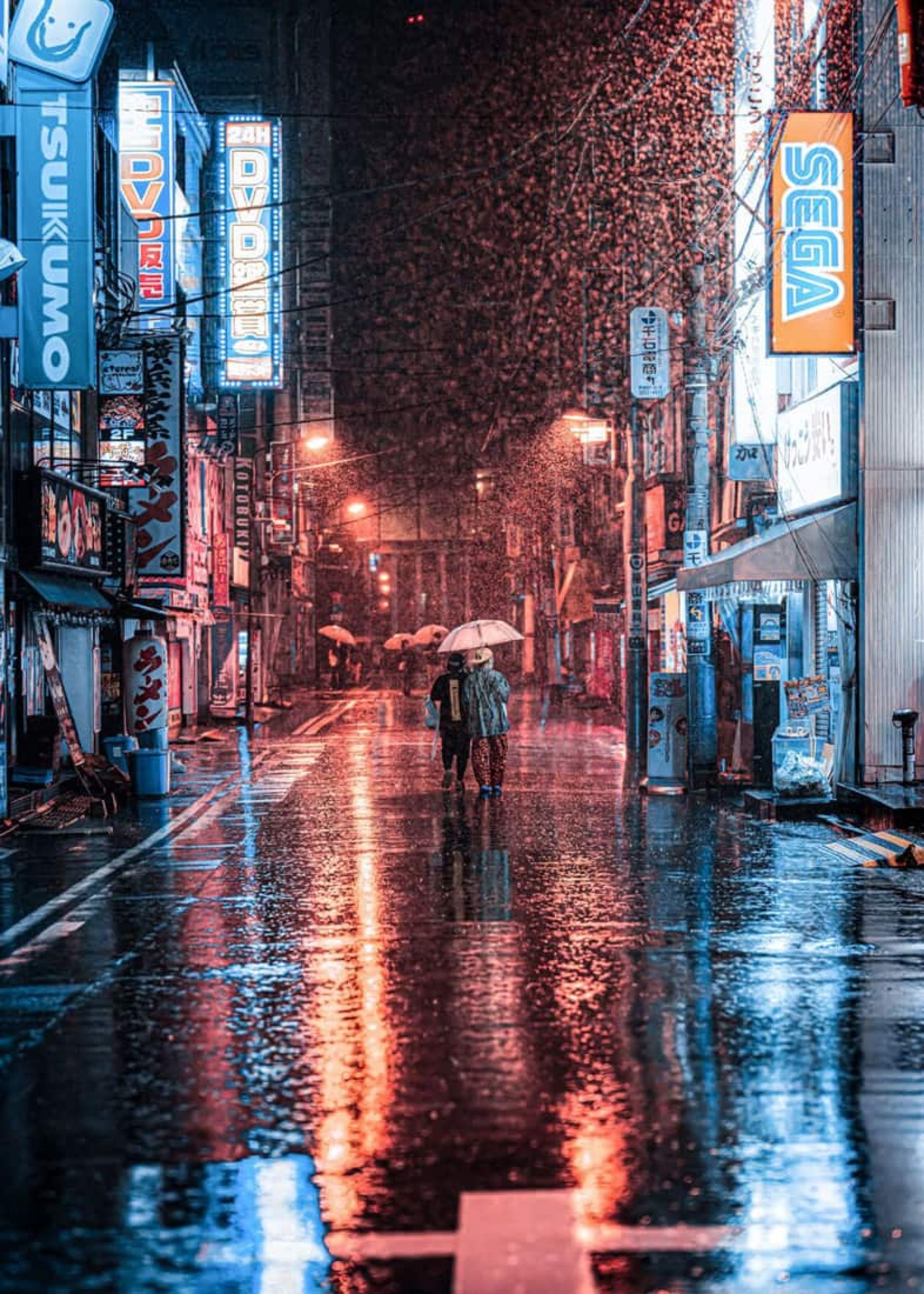 دو نفر با چتر در خیابان بارانی آکیهابارا توکیو در شب