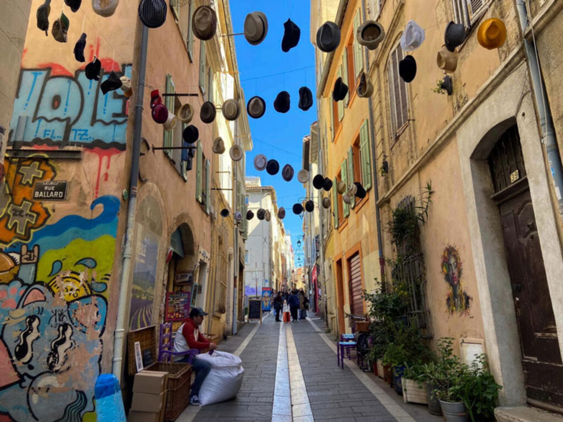 خیابان رنگارنگ محله Le Panier مارسی با کلاه‌های آویزان و دیوارنگاره