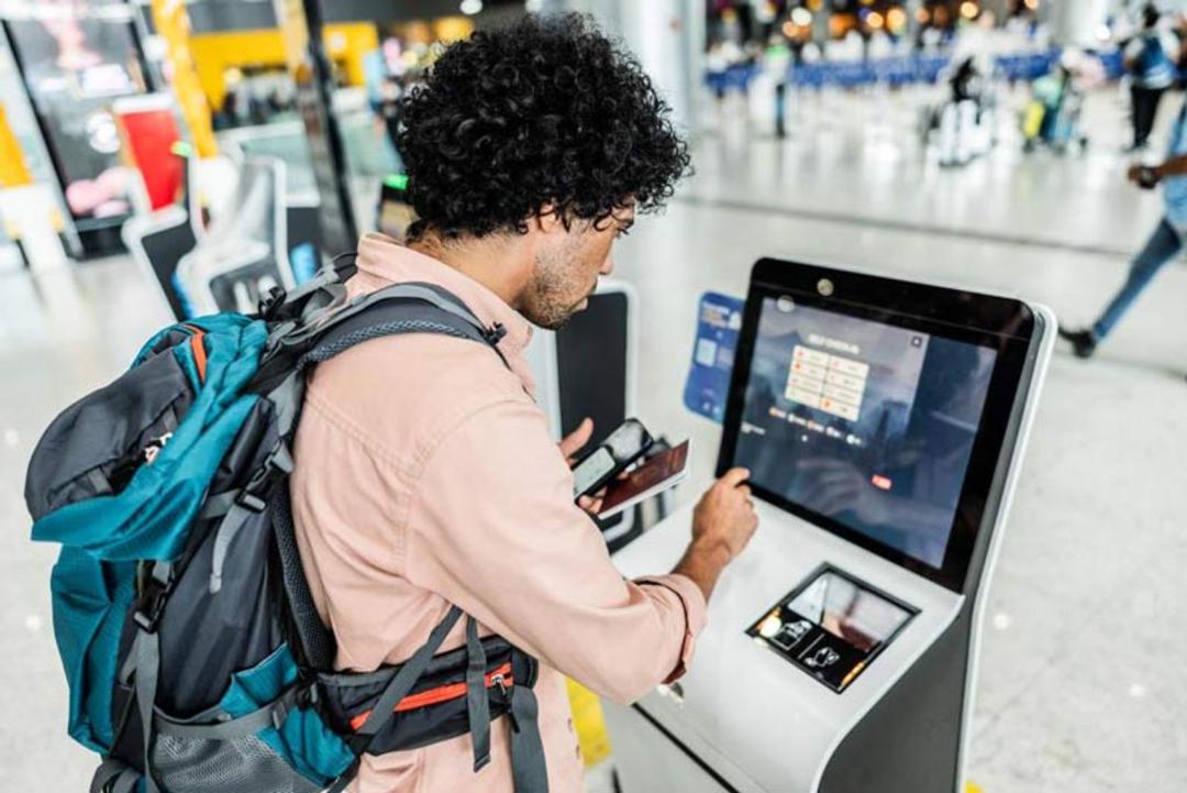 مسافری در حال کار با مانیتور لمسی کیوسک پذیرش (Check-in) برای دریافت کارت پرواز