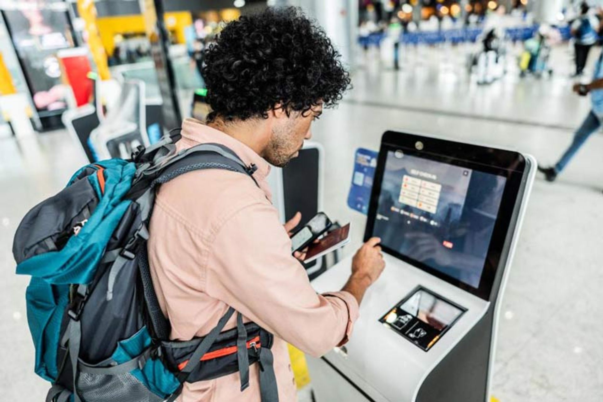 مسافری در حال کار با مانیتور لمسی کیوسک پذیرش (Check-in) برای دریافت کارت پرواز