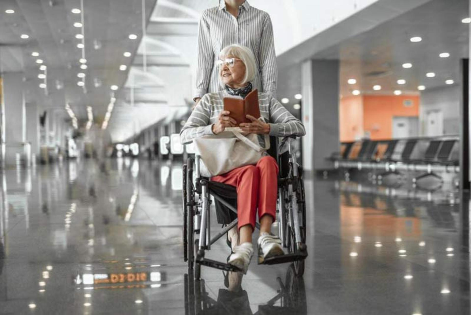 خانم سالخورده روی صندلی چرخ‌دار (Wheelchair) با مدارک سفر در دست در سالن مدرن ترمینال