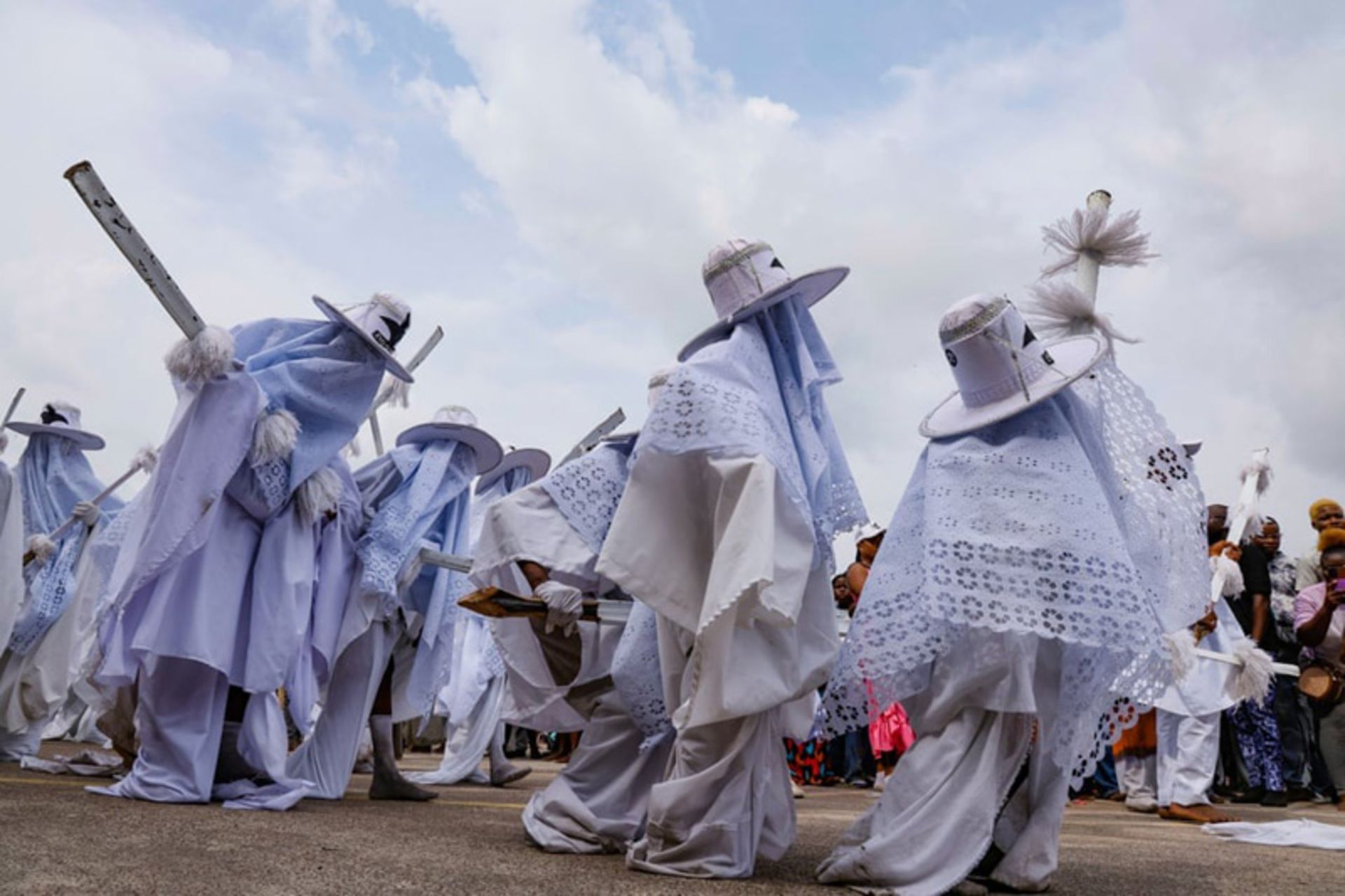 شرکت‌کنندگان با لباس‌های سفید و کلاه‌های لبه‌پهن در جشنواره سنتی «ایو» (Eyo) در لاگوس، نیجریه