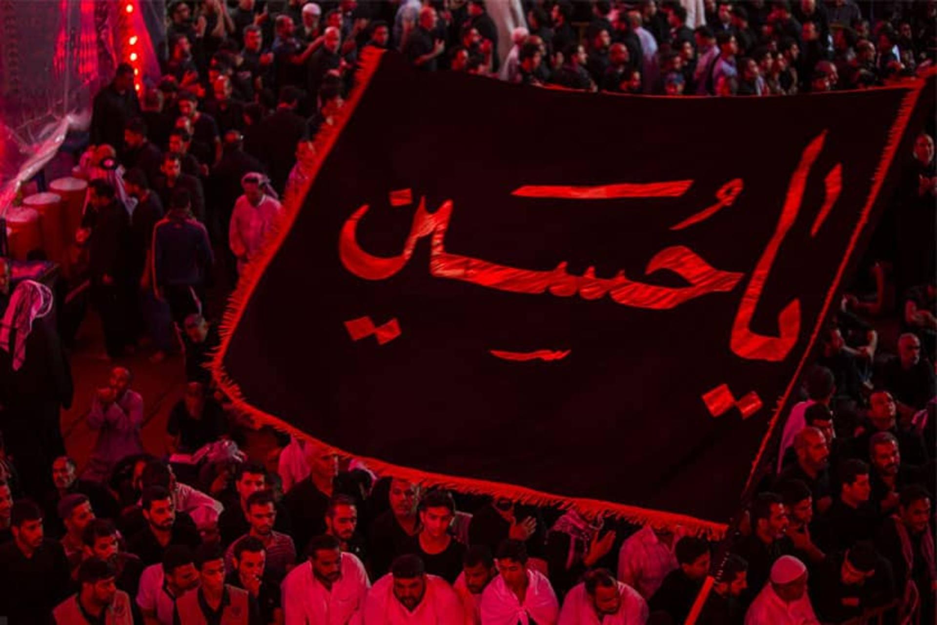پرچم بزرگ یا حسین در میان جمعیت زیادی از عزاداران در نورپردازی قرمز