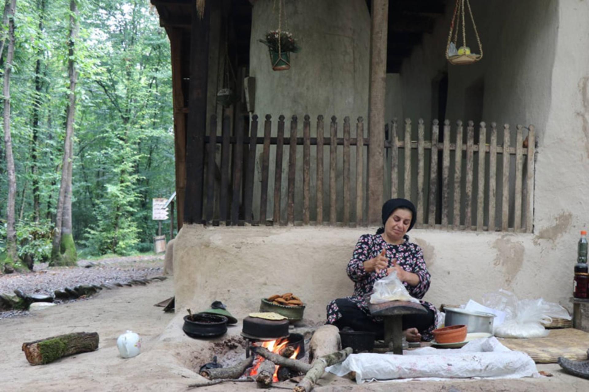 زن روستایی در حال نانوایی با اجاق هیزمی در فضای باز