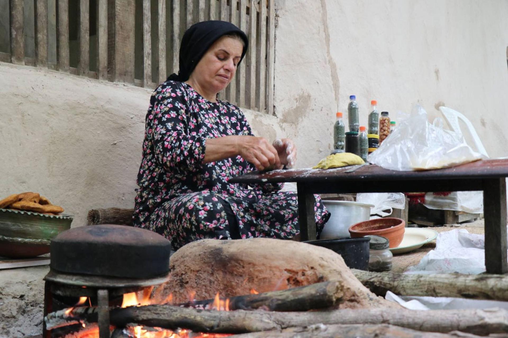 زن روستایی در حال پخت نان سنتی بر روی اجاق هیزمی در فضای باز