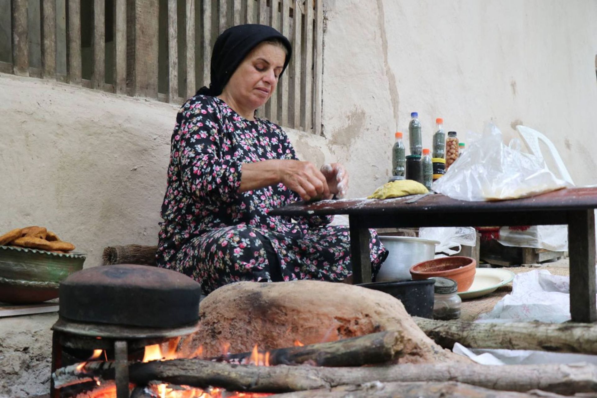زن روستایی در حال پخت نان سنتی بر روی اجاق هیزمی در فضای باز