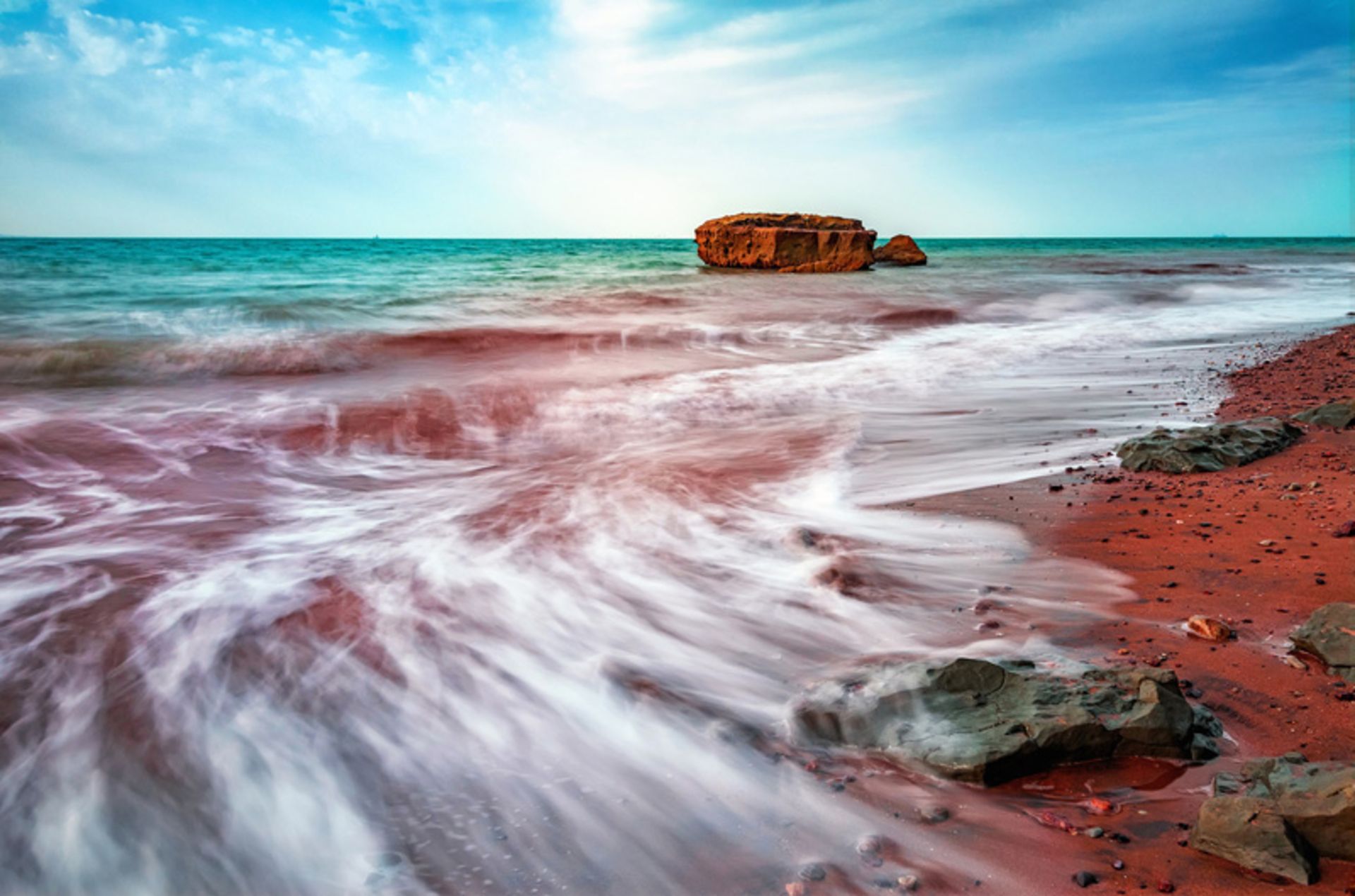 ساحل ماسه‌ای قرمز و موج‌های سفید آب در جزیره هرمز