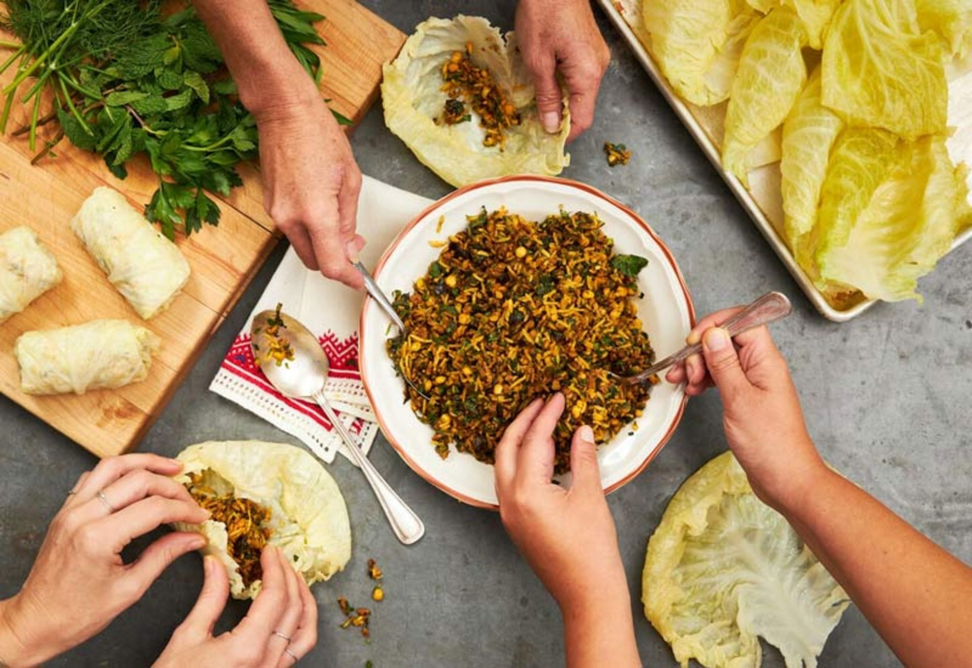 نمای از بالا از چندین نفر در حال پر کردن و پیچیدن دلمه کلم با مواد میانی گوشت و سبزیجات