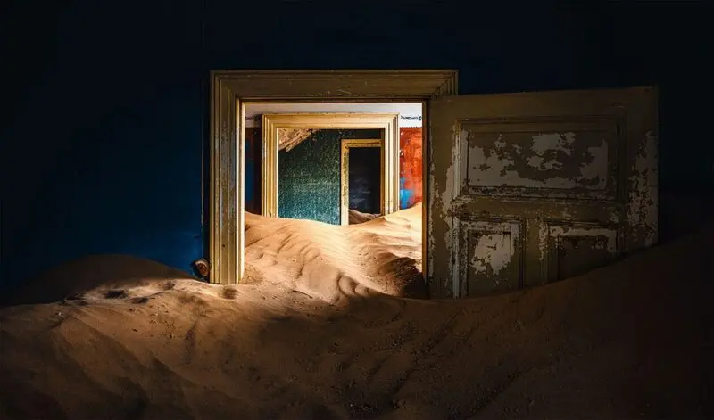 شن‌های بیابان در میان درهای باز خانه‌های متروکه کولمانسکوپ (Kolmanskop)
