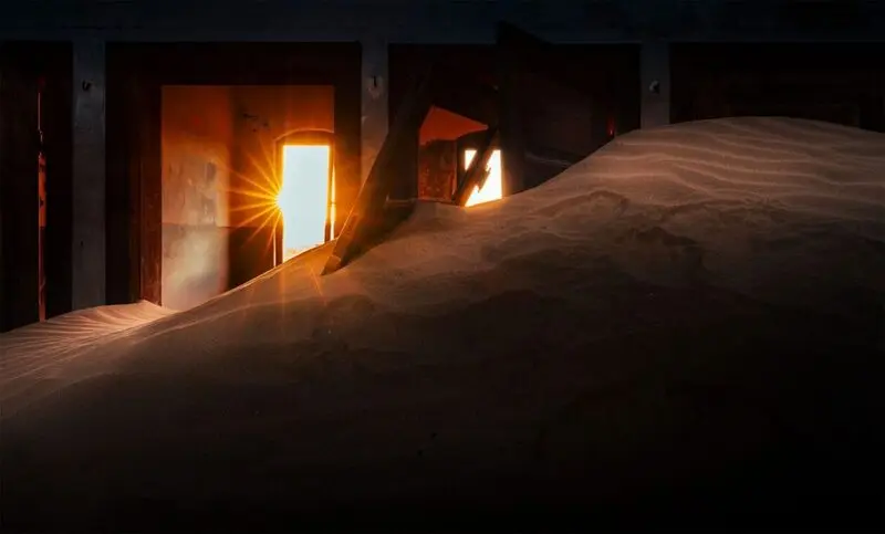 شن‌های بیابان در داخل ساختمان‌های متروکه شهر کولمانسکوپ (Kolmanskop) با نور خورشید