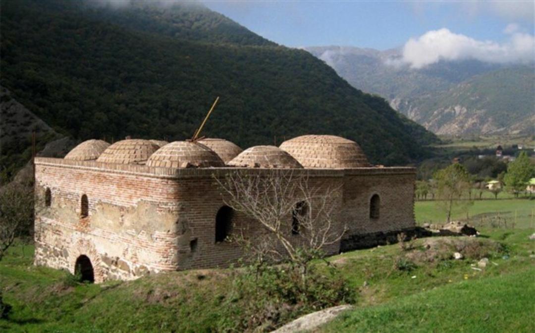 بنای قدیمی با چندین گنبد آجری در دل طبیعت کوهستانی
