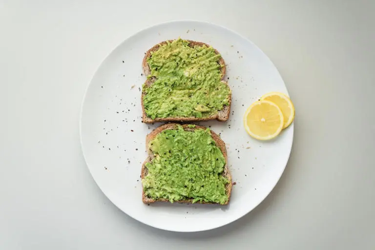 نان تست با آووکادو (Avocado) و برش‌های لیموترش روی بشقاب سفید
