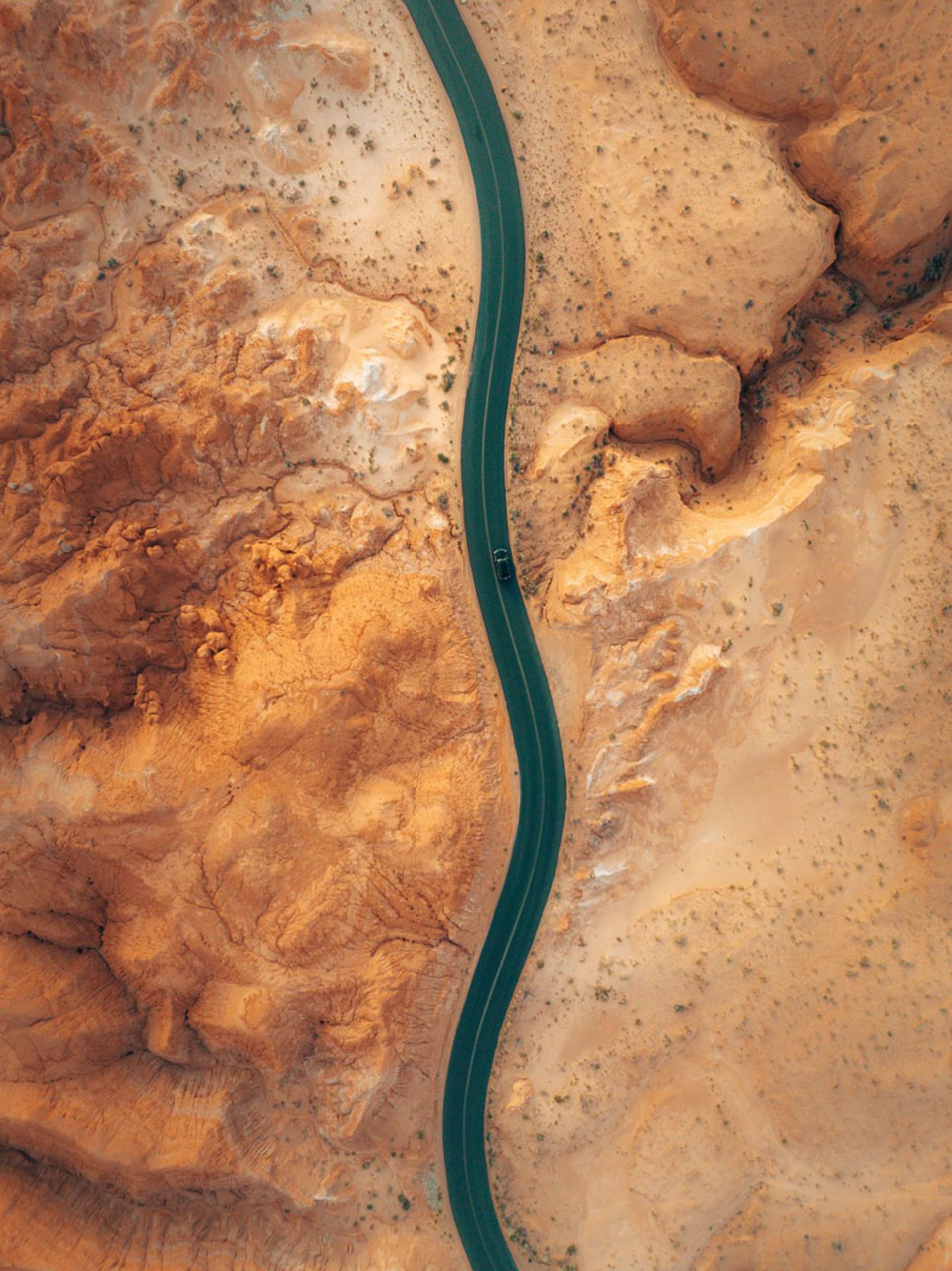 عکس هوایی از جاده‌ای سیاه و مارپیچ در میان دشت‌های کویری