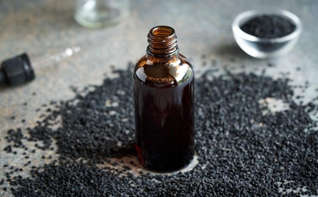 روغن سیاه‌دانه (Black Seed Oil) در یک بطری شیشه‌ای تیره روی دانه‌های سیاه‌دانه