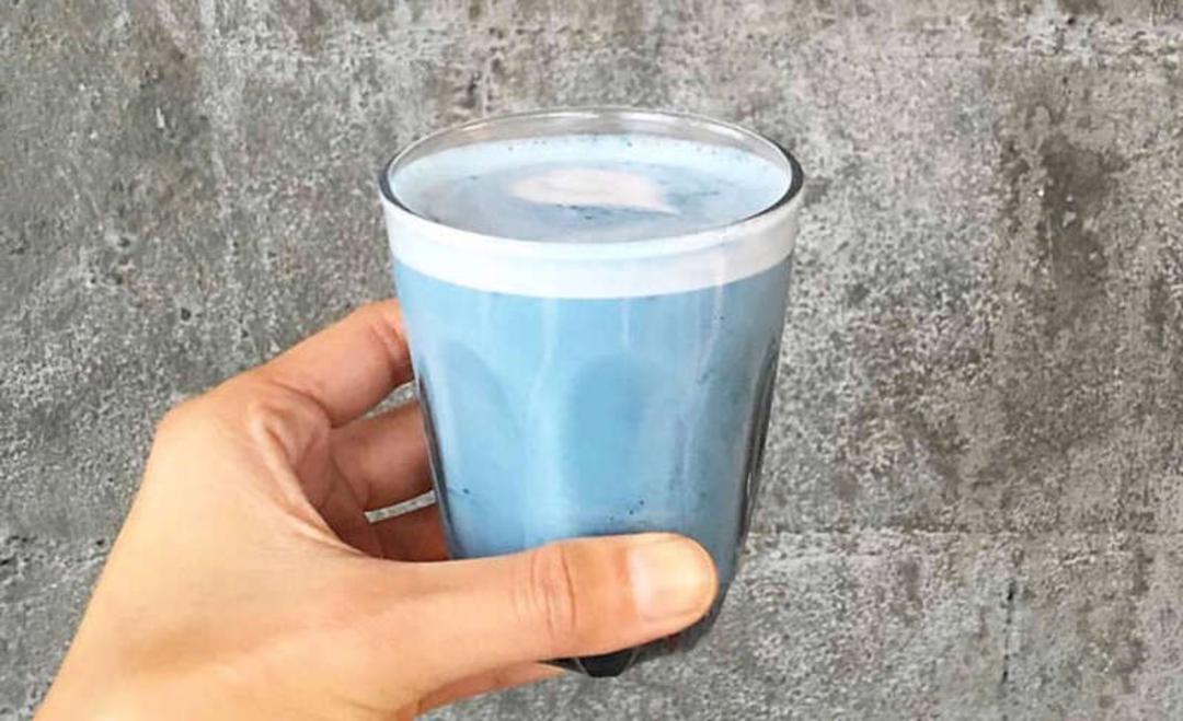 نوشیدنی آبی رنگ در یک لیوان شیشه‌ای در دست فرد