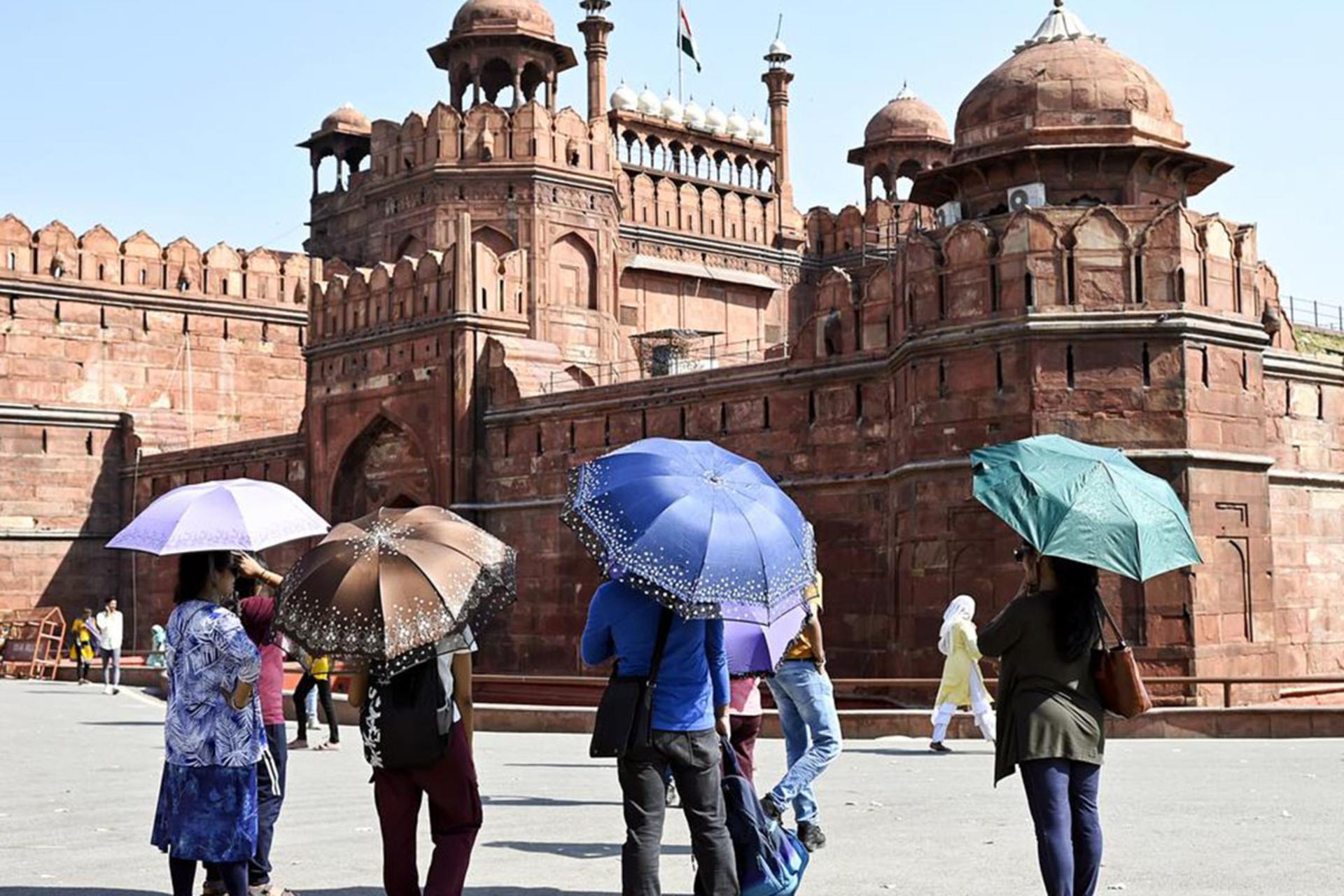 نمای از پشت سر گروهی از گردشگران با چترهای رنگی در مقابل بنای تاریخی و عظیم «قلعه سرخ»
