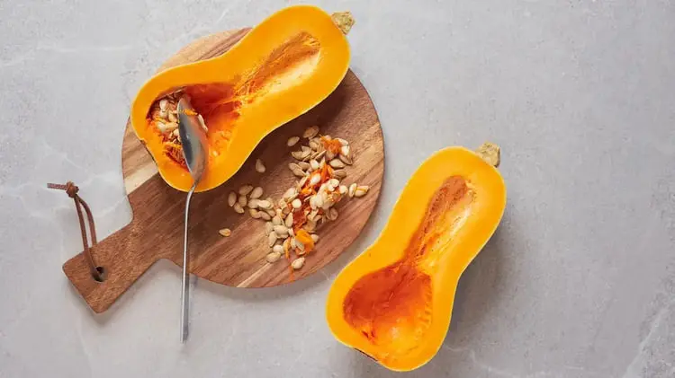 کدو حلوایی (Butternut Squash) نصف شده همراه با دانه‌های آن روی تخته چوبی