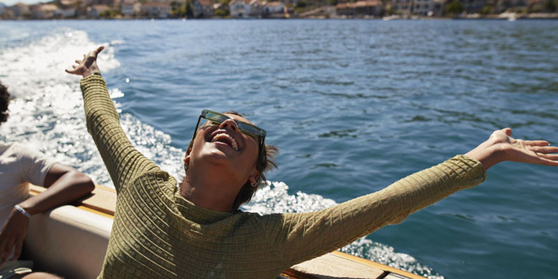 زن خوشحال با عینک آفتابی، دستانش را روی قایق به آسمان باز کرده
