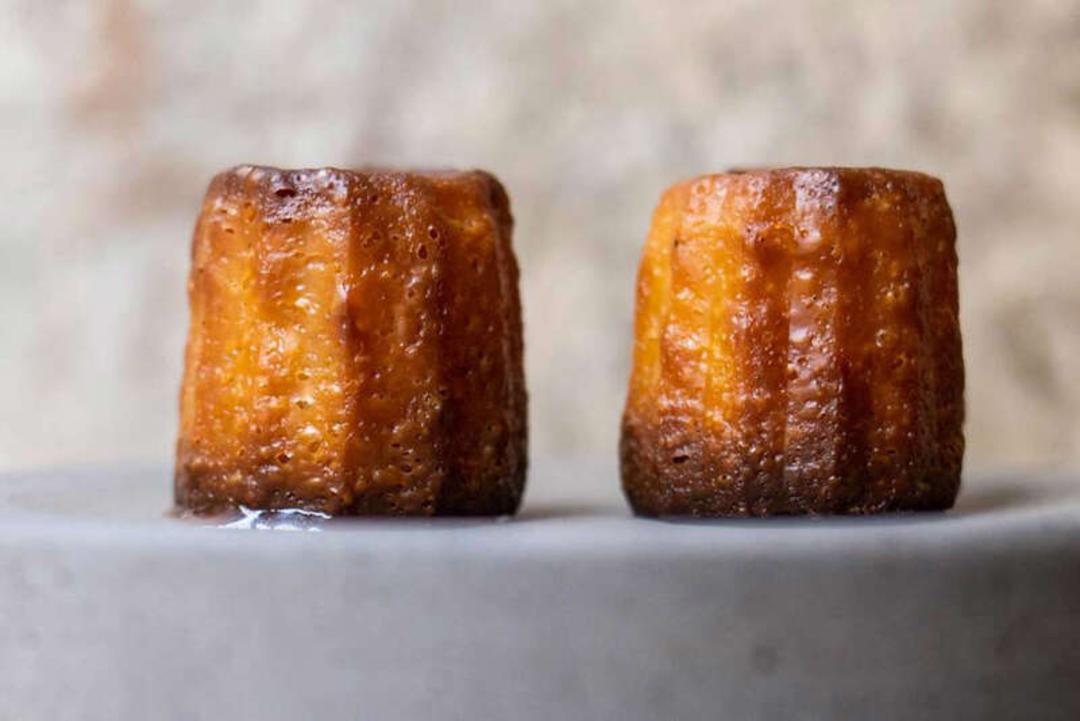 دو عدد شیرینی کانیله (Canelé) با پوست ترد و کاراملی روی بشقاب