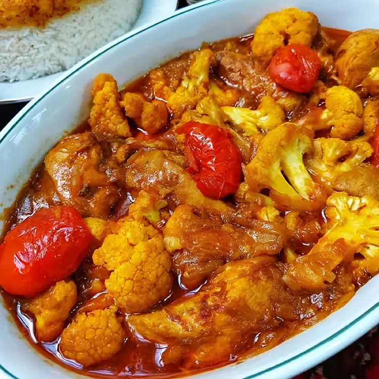 خورش گل کلم (Cauliflower) همراه با تکه‌های گوشت و گوجه‌فرنگی در ظرف سفید
