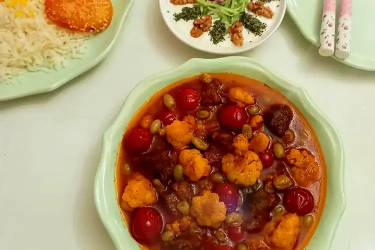 خورش گل کلم (Cauliflower Stew) حاوی تکه‌های گوشت، گوجه‌فرنگی و کشمش در ظرف سبز